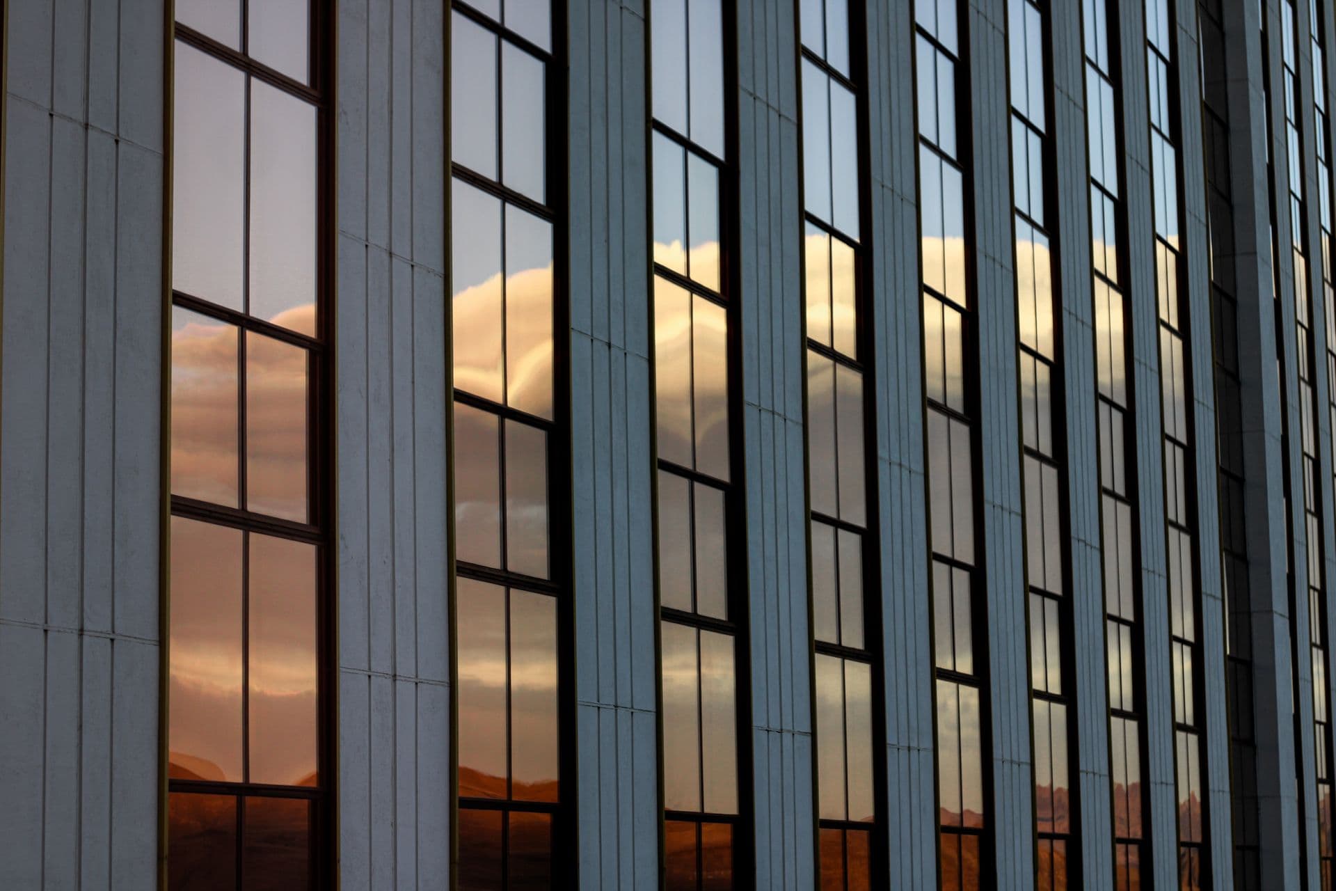 A tall glass curtain wall in Reno, Nevada reflecting sunset clouds and the mountains behind the photographer across dozens of window panes.