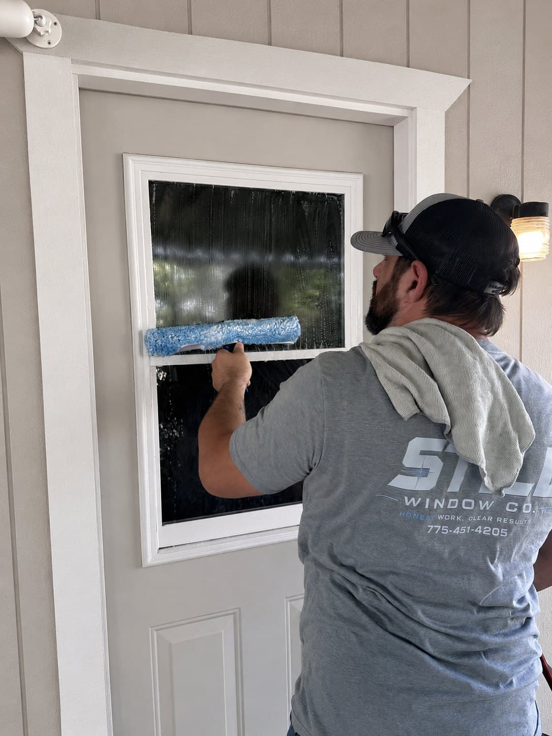 Still Window Co squeegeeing the glass pane of a residential door, working the blade along the frame and sill.