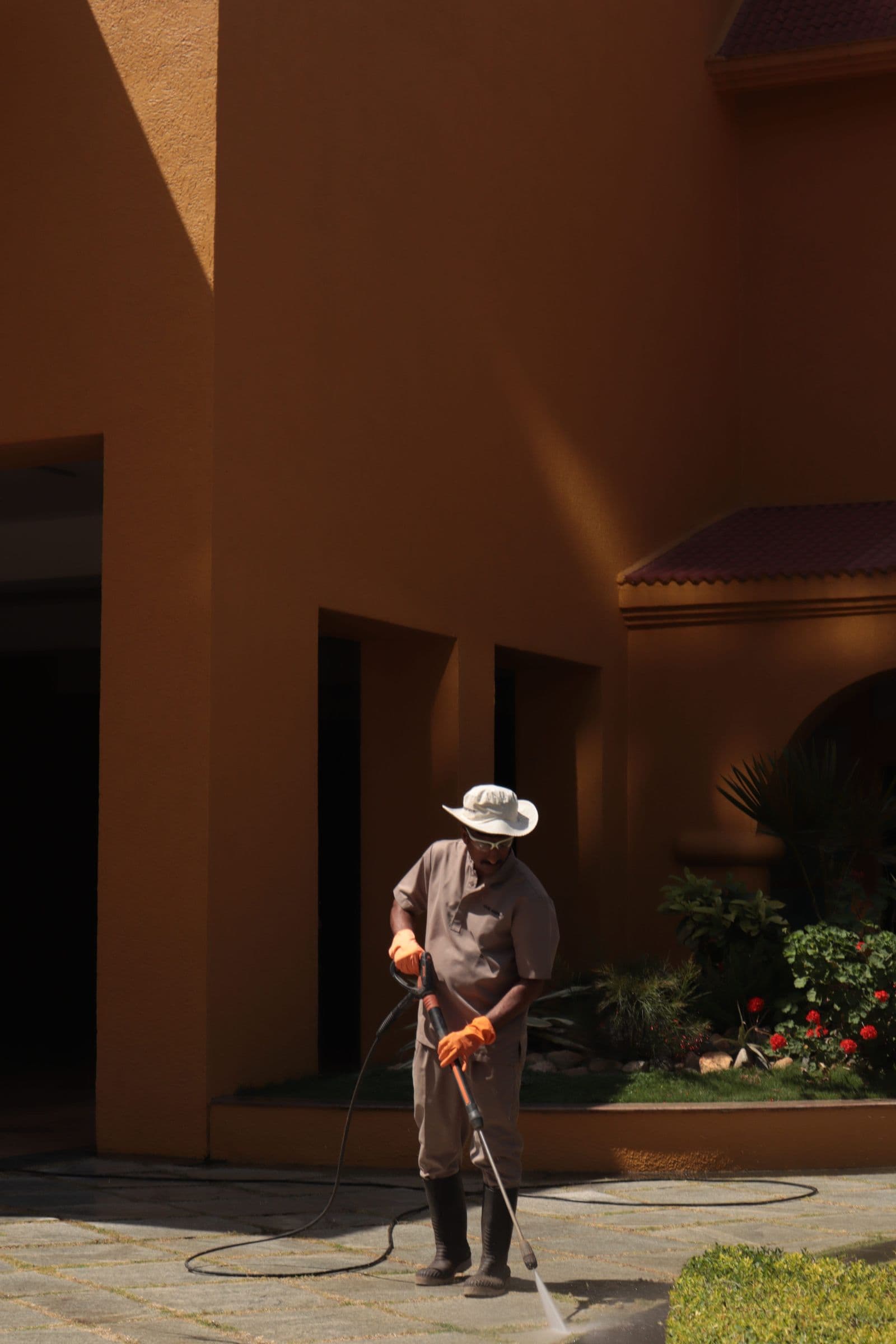 Worker pressure washing a stucco building's patio walkway, clearing built-up high-desert dust and grime.
